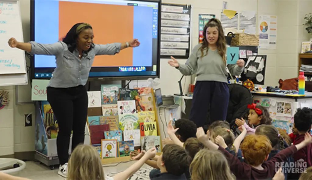 Two teachers working with students who are sitting on the floor.