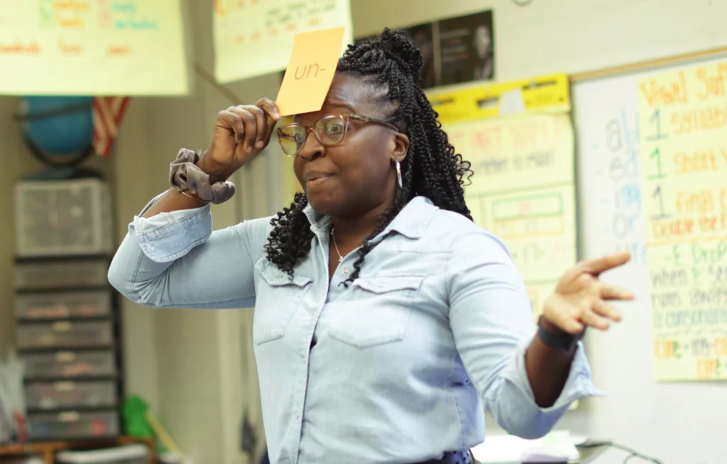 Teacher holding a flashcard for the prefix 'un-' to her forehead.