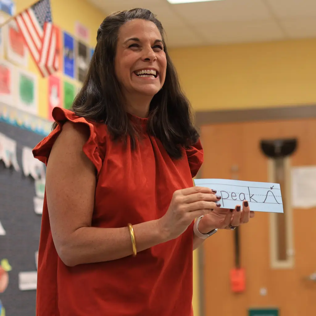 Smiling teacher holding up a flash card for vowel team and diphthongs lesson.