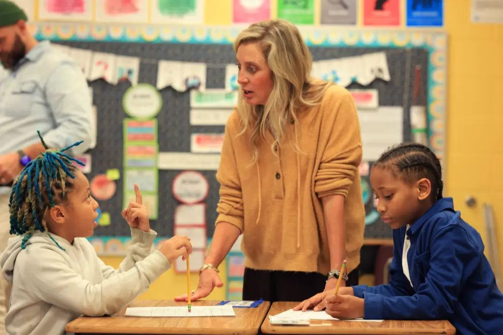 A teacher talking with students at their desks.