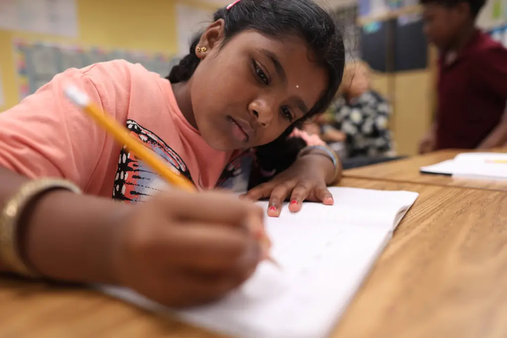 Young student writing in a notebook at her desk.