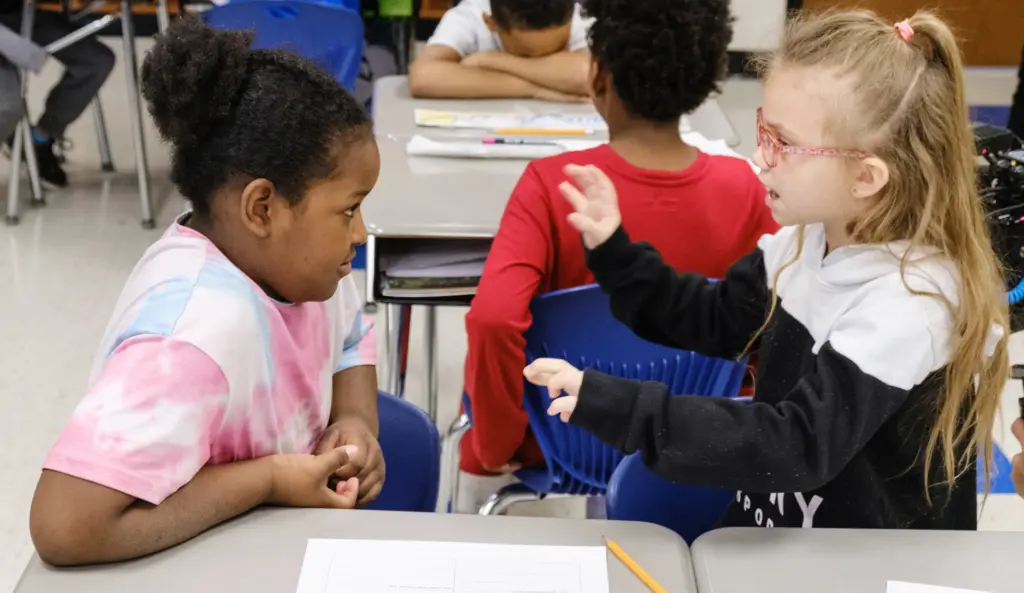 Two young students at their desk having a discussion.