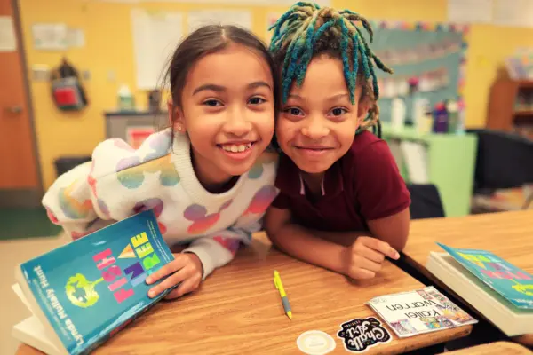 Two smiling young students holding books.