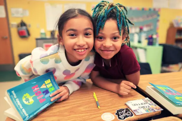Two smiling young students holding books.