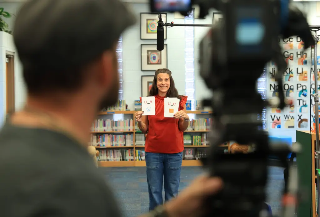 A teacher being filmed while holding flash cards.